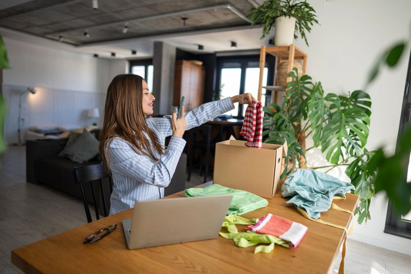 Young woman entrepreneur working from home, capturing images of her handmade clothing for an online store, blending creativity with modern technology in a cozy home office setting