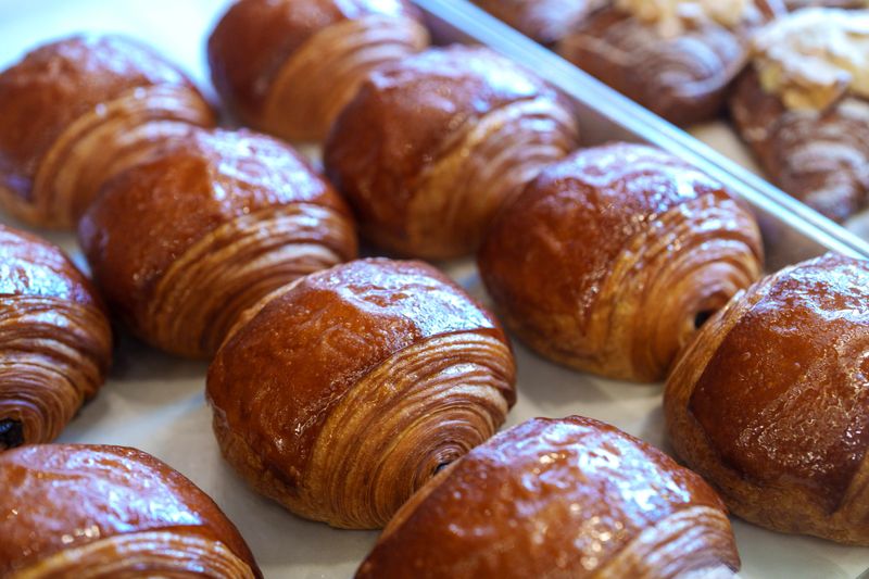 Rows of golden brown pain au chocolat pastries displayed on a baking tray at a local bakery, showcasing their glossy, flaky layers.