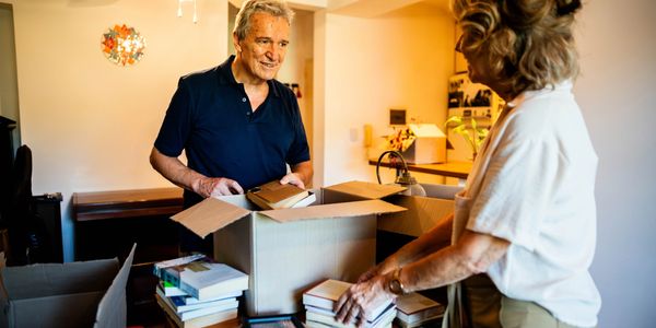 Older couple packing books into moving boxes in a cozy home.