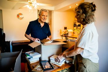 An elderly couple packing books into boxes in a cozy home.