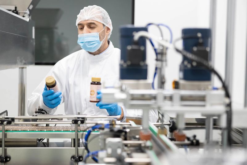 A focused worker in a clean room environment examines dietary supplements, showcasing production and quality control processes.