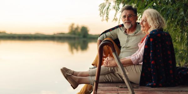Elderly couple sitting on dock by a calm lake at sunset.