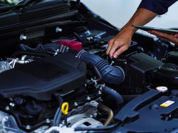 Hand inspecting a car engine compartment.