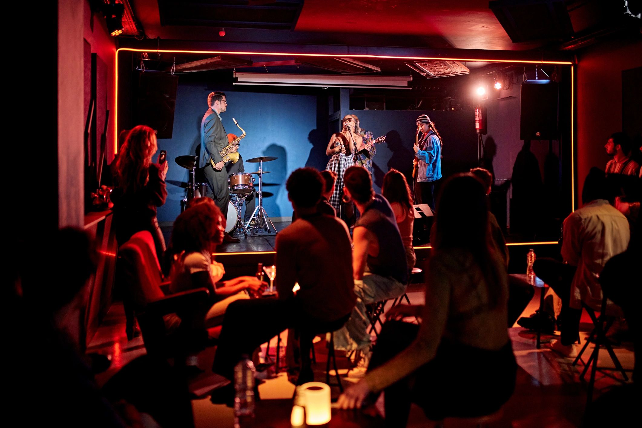 Live band performing on stage in a dimly lit club with an engaged audience.