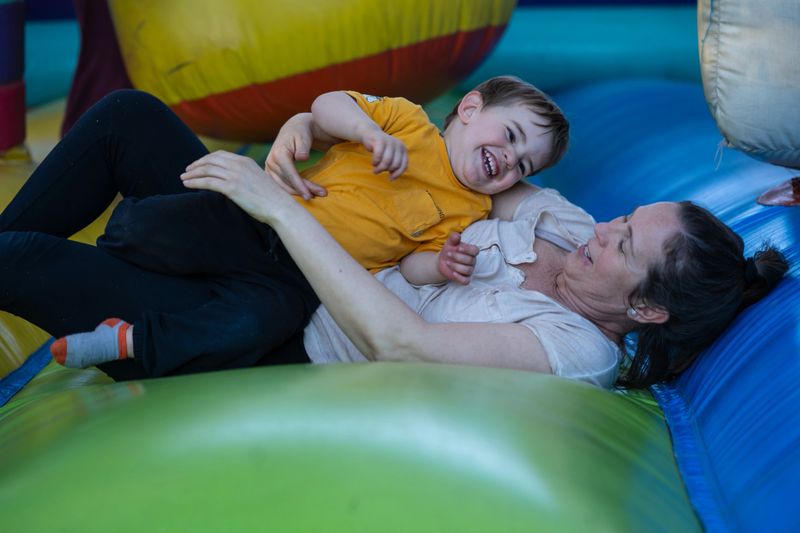 Mother and son laughing and playing together on a colorful inflatable bouncy castle, enjoying quality time and creating happy memories