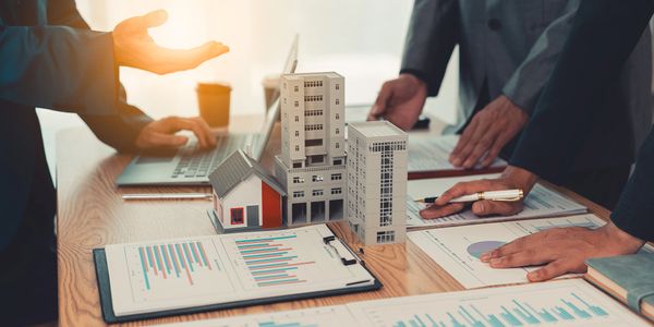 Business meeting discussing real estate investments with building models and charts.