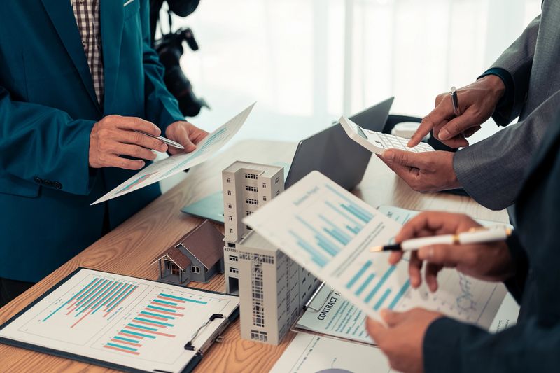 Real estate entrepreneurs meeting to sell a house, discussing real estate deals, with house plans on the table, symbolizing real estate investment and negotiations.