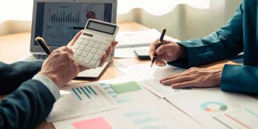 Two people analyzing financial data with a calculator and charts.