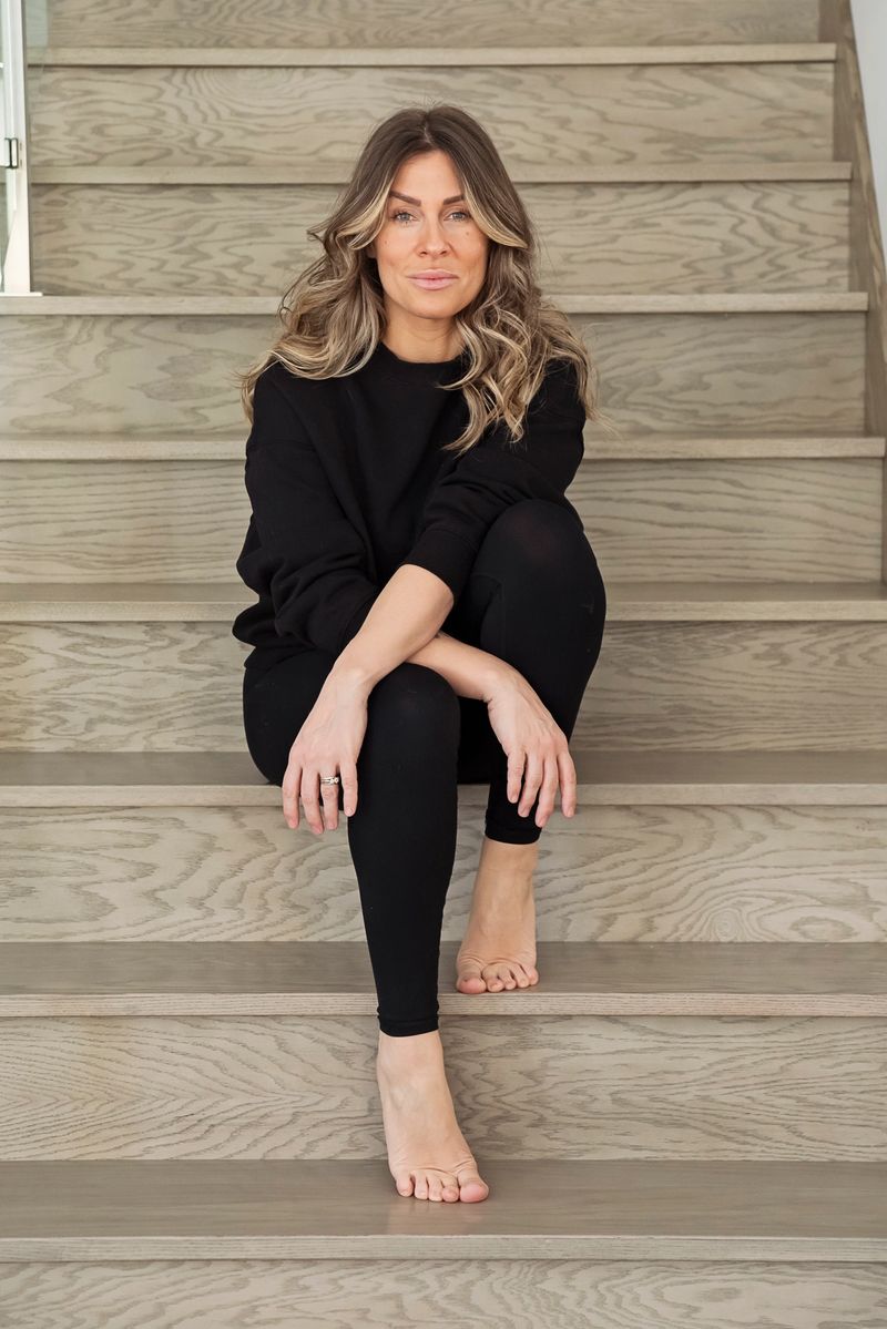 Portrait of confident woman in staircase. She is in her forties, with long hair, a black sweater and black leggings. Vertical full length indoors shot . This is part of a series « day in the life » taken in Quebec, Canada.