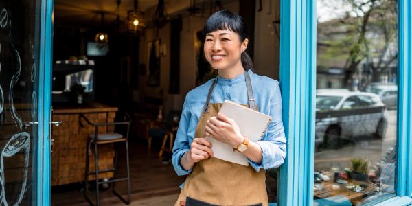 Smiling woman standing at a doorway holding a notebook.