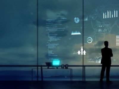 Silhouette of a person analyzing digital data on a large screen in a dark office.
