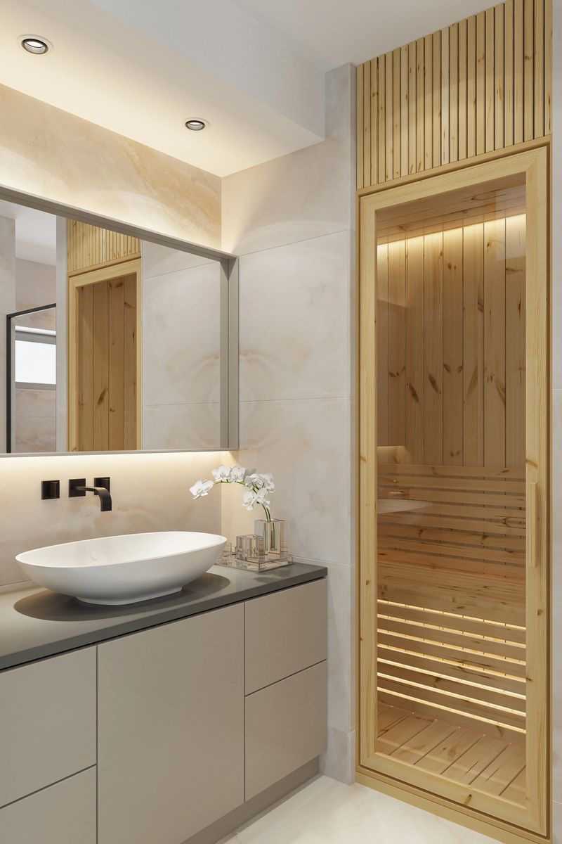 This luxurious home spa bathroom combines modern elegance with natural wellness elements. The space features large marble stone tiles that bring a sense of refinement and timeless style. A Finnish sauna crafted from natural pine wood adds warmth and relaxation, softly illuminated with ambient yellow lighting for a calming atmosphere. The bathroom includes a spacious vanity with an oval vessel sink, a wall-mounted faucet, and a round mirror, creating a harmonious and functional design. Subtle ceiling strip lights and classic spotlights enhance the mood with soft golden tones, completing this sophisticated wellness retreat.Ideal for showcasing high-end bathroom design, residential spas, and luxury home features.