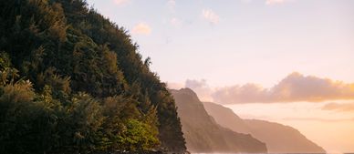 Sunset over lush cliffs by the ocean with gentle waves.