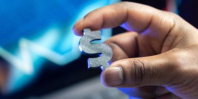 Hand holding a metallic dollar sign symbol.