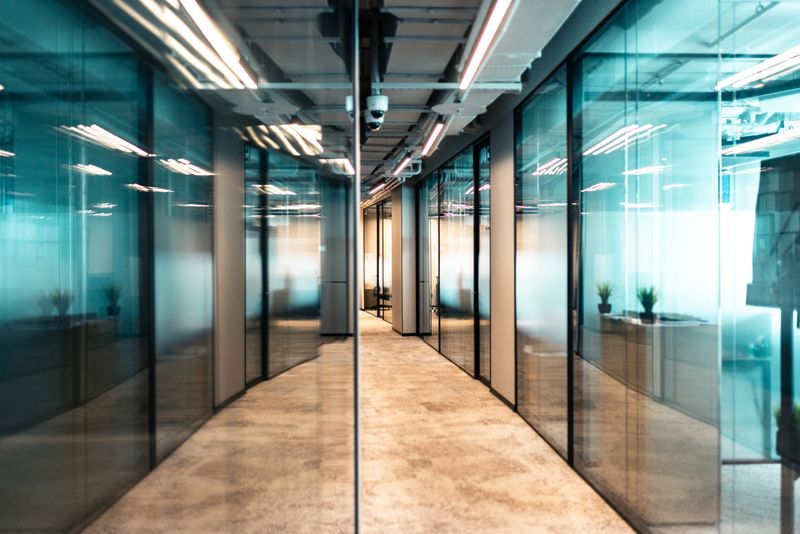 Bright and spacious interior design of a contemporary office hallway, featuring glass partitions and modern lighting fixtures, providing a professional and organized work environment.
