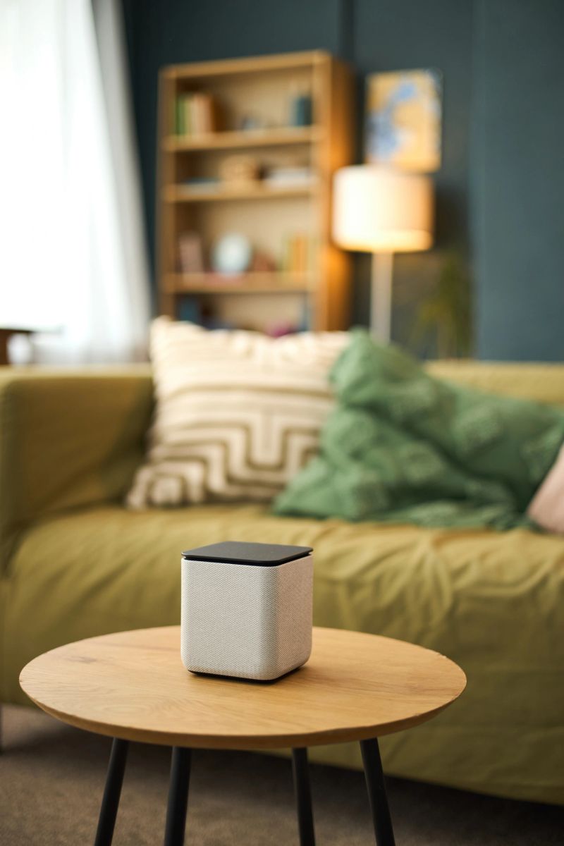 Modern smart speaker placed on round wooden table against backdrop of contemporary living room, enhancing decor with sleek design and functionality
