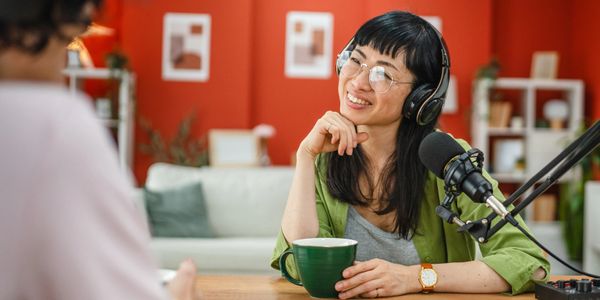 Smiling woman with headphones and microphone enjoys podcast recording.