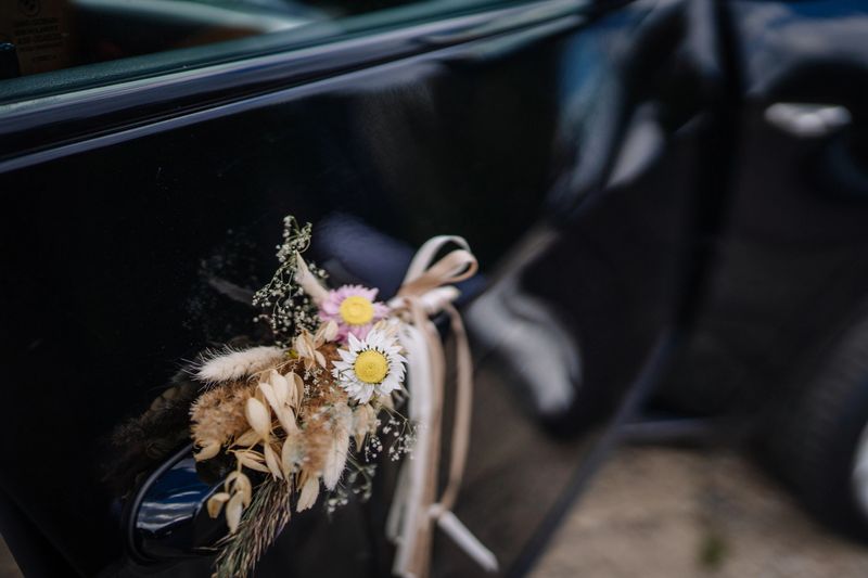 Valmiera, Latvia - August 9, 2024 - A delicate floral wedding decoration with ribbons and dried flowers is attached to the handle of a black car, symbolizing a special occasion.