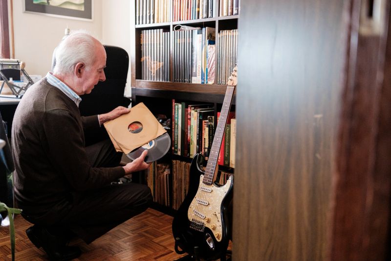 Senior man carefully selecting a vinyl record from his extensive music collection, with a guitar nearby