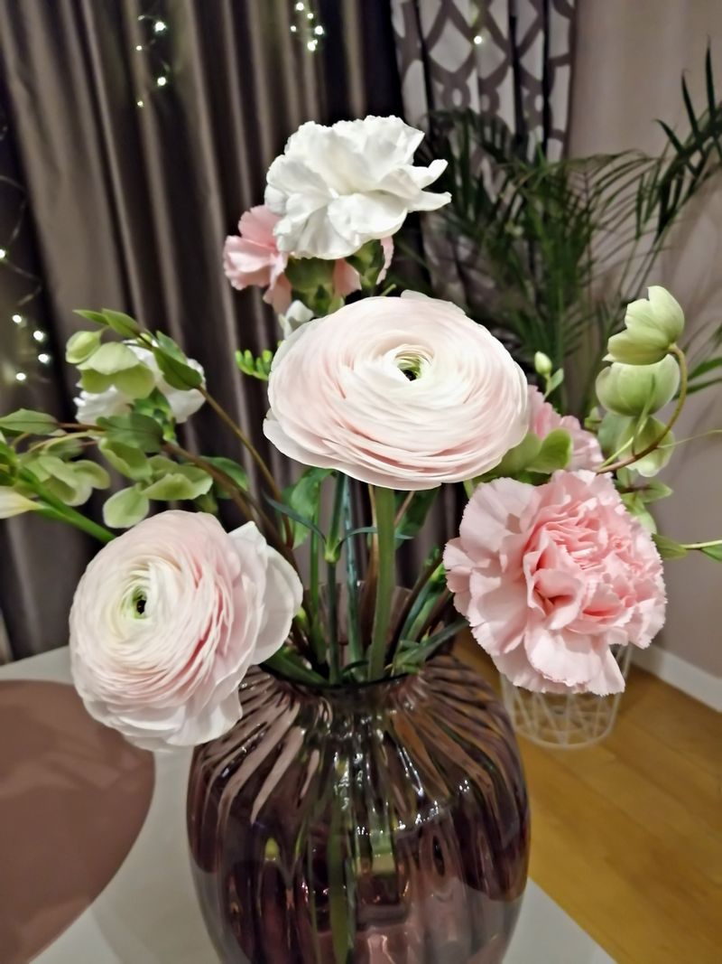 Refined bouquet of pastel ranunculus, carnations and freesia in glass vase on table in cozy interior. Ideal for interior design or spring themed. Elegant flower bouquet in glass vase. Vertical