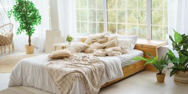 Cozy unmade bed in bright, airy room with plants.