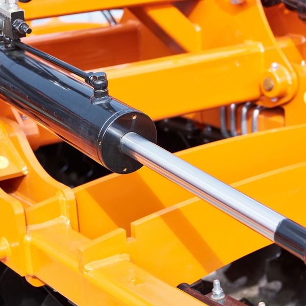 Close-up of a hydraulic cylinder on bright orange machinery.