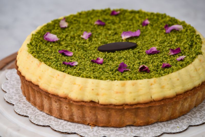 Pistachio Tart, featuring a creamy filling with pistachio topping, garnished with rose petals and a chocolate piece closeup side view of flavorful baked dessert