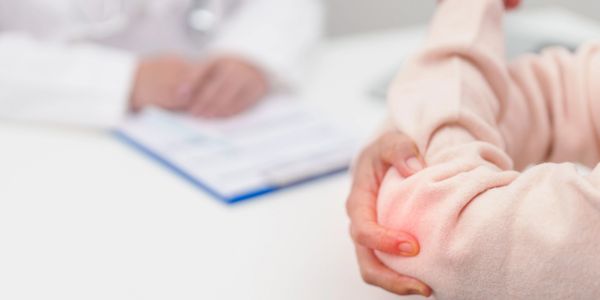 Patient holding elbow with doctor in background.