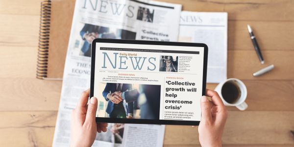 Person reads digital newspaper on tablet with coffee nearby.