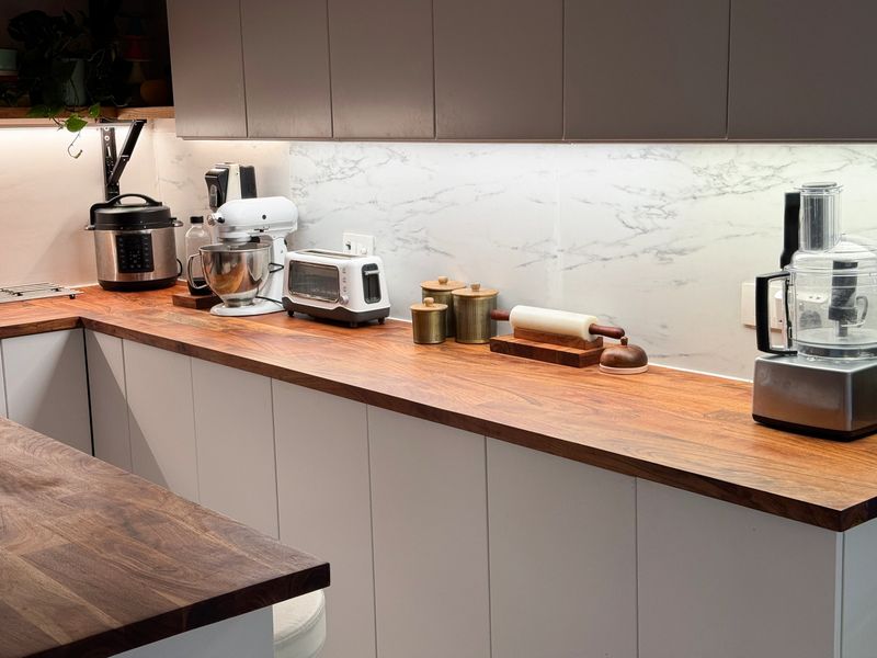 Stock photo shows a contemporary kitchen features sleek wooden worktops and countertops, paired with stylish flooring. The space is beautifully illuminated with under cupboard lighting and soft kitchen lights, creating a warm and inviting atmosphere