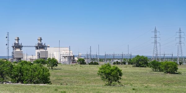 Power plant with transmission towers in a green field under clear blue sky.