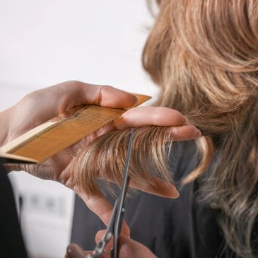 Hairdresser cutting brown hair with scissors and comb.