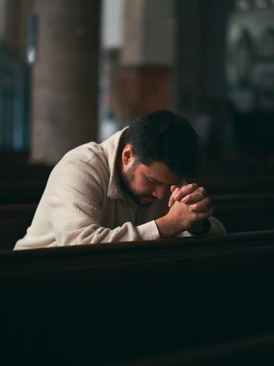 Man praying alone in a dimly lit church pew.