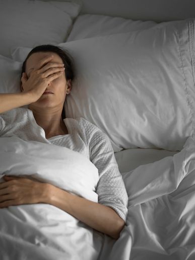 Woman lying in bed with hand on face, appearing stressed or tired.