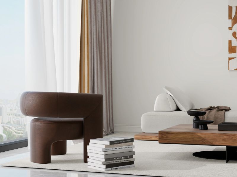 Modern living room with neutral tones, featuring a beige sofa with green and polka dot pillows, a round coffee table, and contemporary wall art. Large windows with sheer and gray curtains create a bright and inviting space.