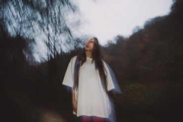 A woman in a white dress standing in a blurred forest background.