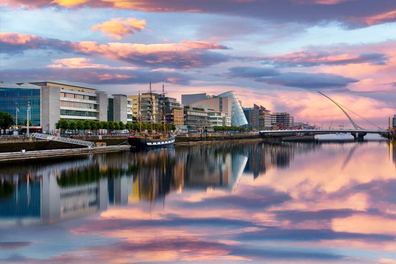 Modern buildings line the River Liffey in Dublin, Ireland, and the iconic harp-shaped Samuel Beckett Bridge spans the river.