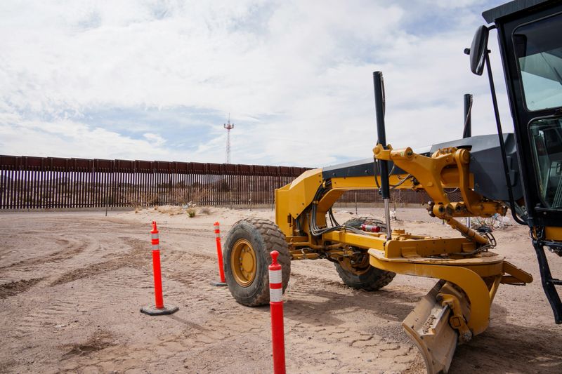 Caterpillar Tractor in Foreground of the Iron Border Wall Between Texas, USA and Chihuahua Mexico on a Clear Early Evening Just Before Sunset