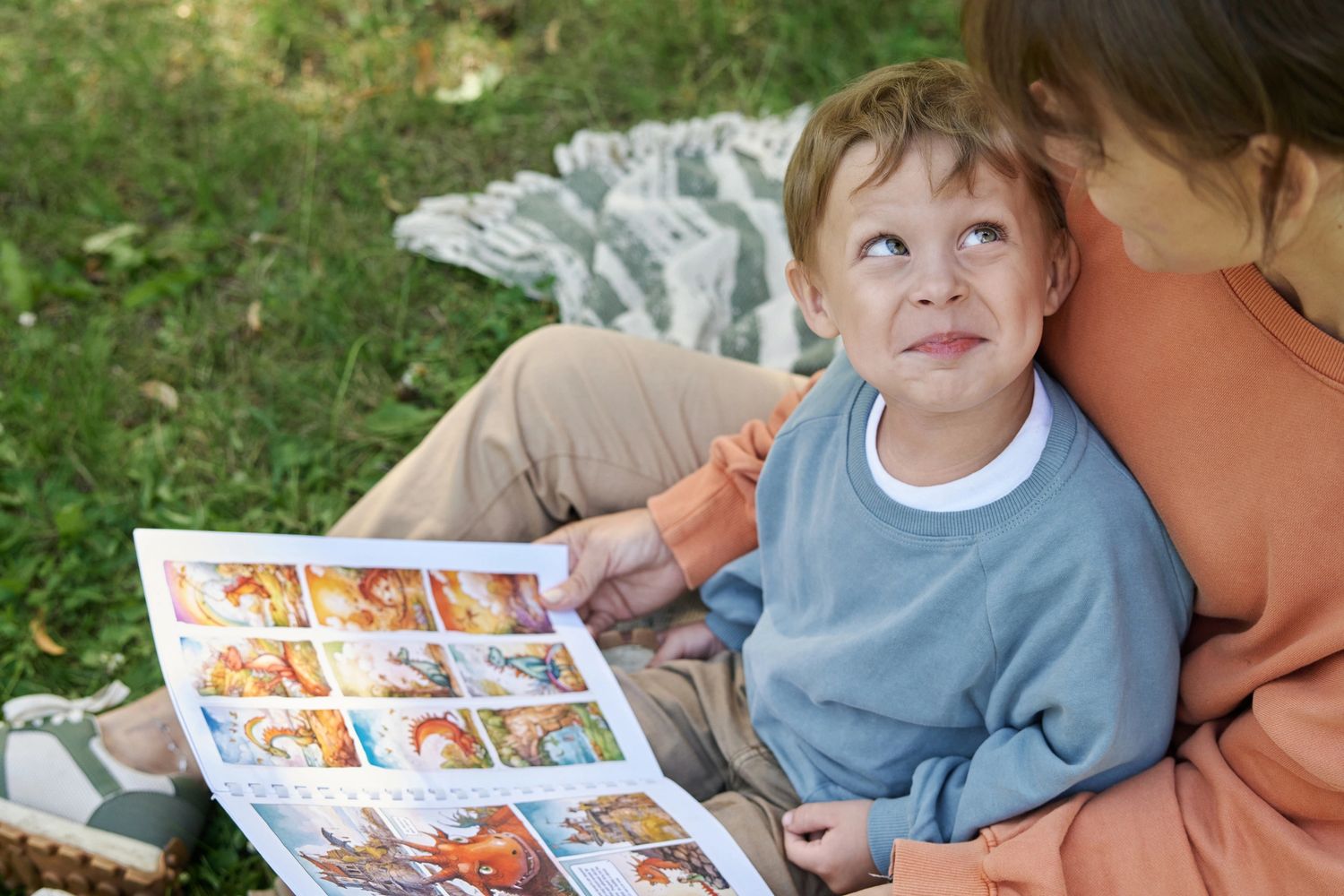A child and adult reading a colorful picture book outdoors on a blanket.