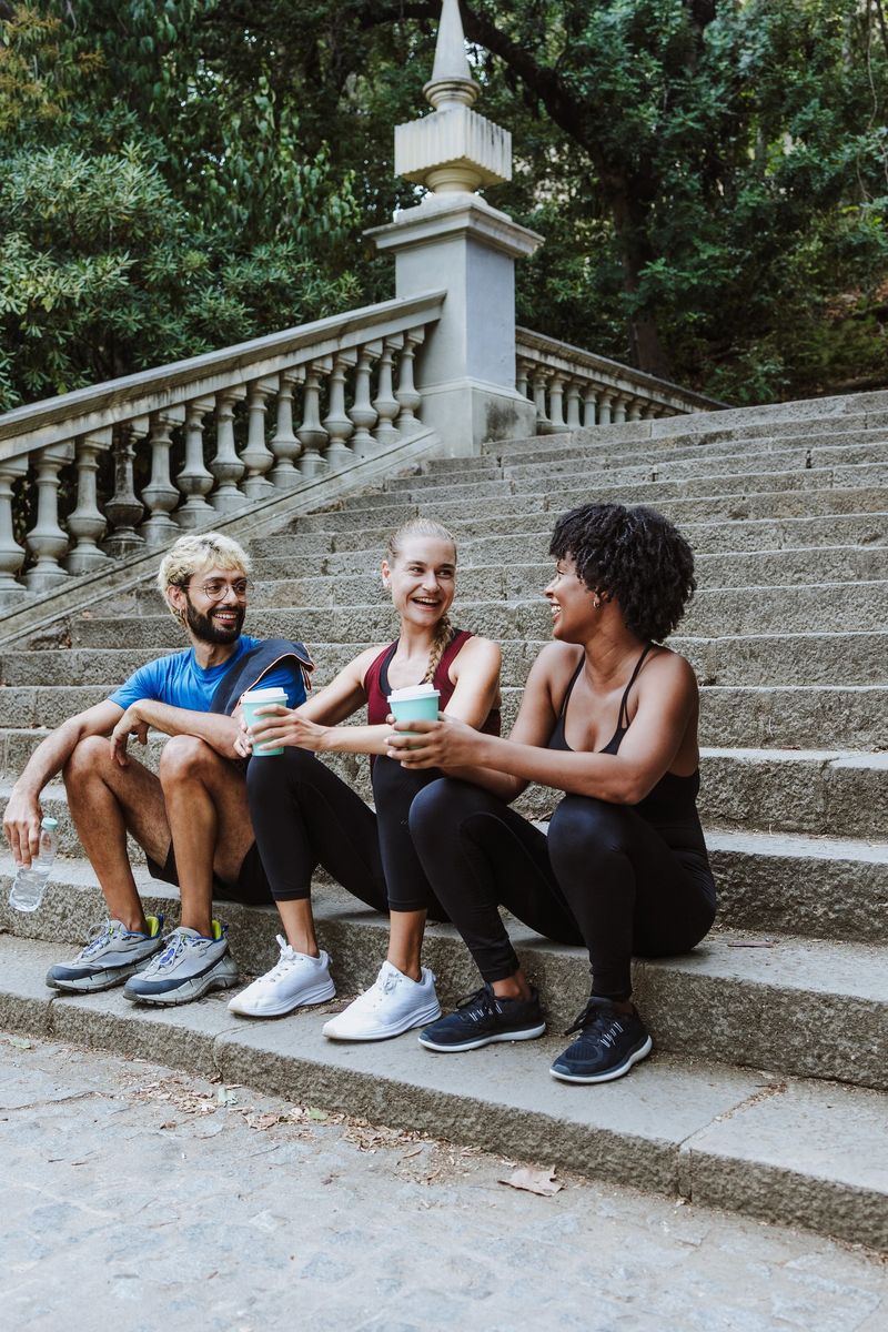 group of multiethnic friends drinking water or coffee and resting after doing exercise together in a City Park in Spain Europe. Hispanic man and afro hair woman wearing athletic clothing