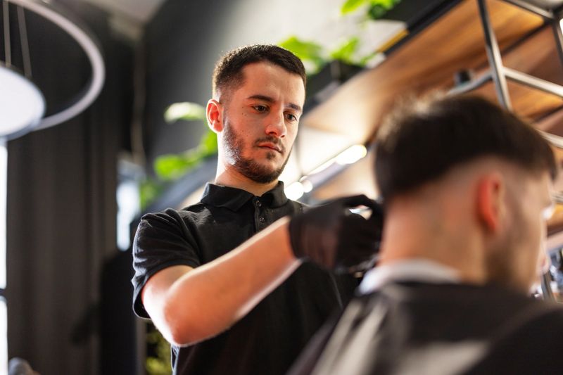 Hairdresser cutting client's hair with electric razor in barber shop
