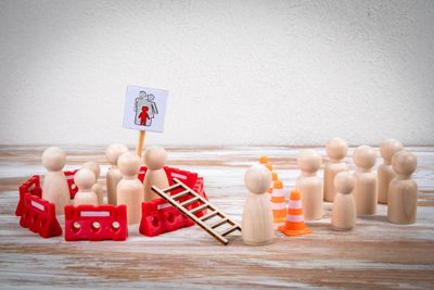 Wooden figures divided by barriers and cones, symbolizing social distancing.
