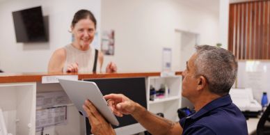 Man assisting woman at a service counter with a tablet.