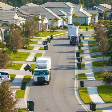 Trash trucks collecting garbage on a suburban street.