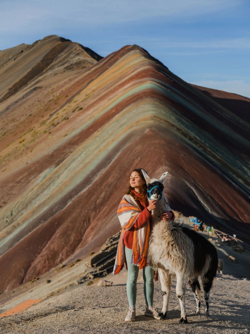 Cheerful woman with alpacas on the background of Rainbow mountain in Peru