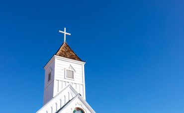 White church steeple with cross against clear blue sky.