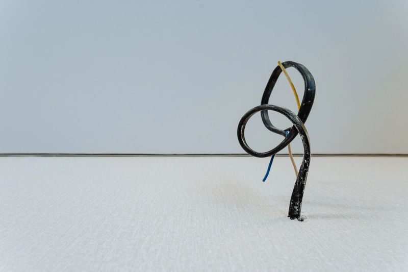 At this moment, a broken wire is lying on an unblemished white surface, which creates a striking contrast that emphasizes its unique features and visible imperfections for all to see