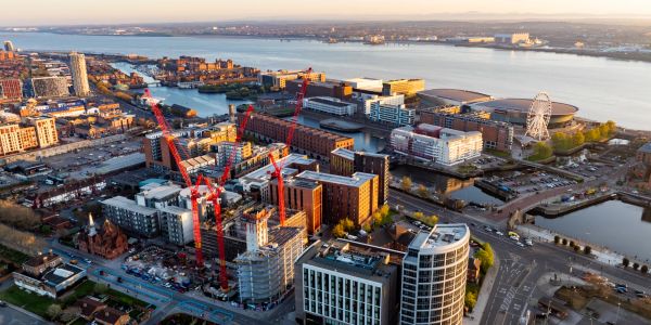 Aerial view of a waterfront city with construction cranes and a large ferris wheel.