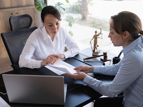 Two women discuss legal documents in a professional office setting.