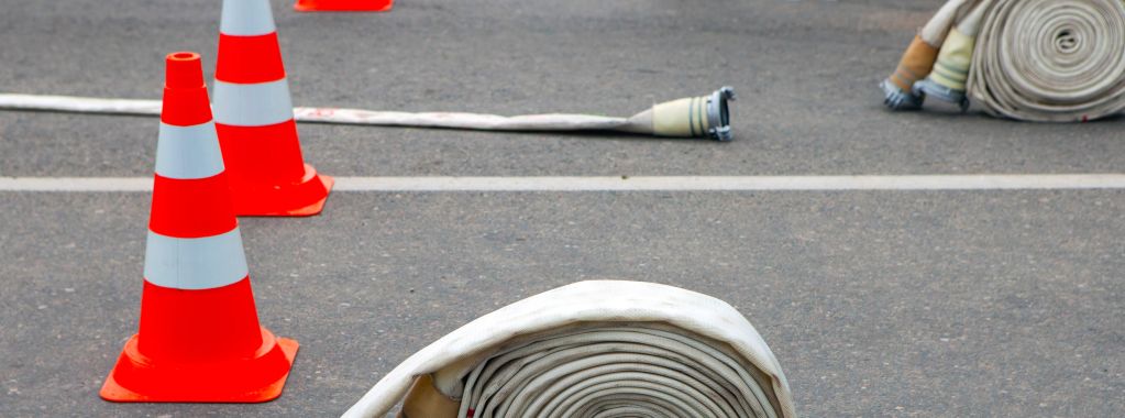 Rolled fire hoses and orange traffic cones on asphalt.